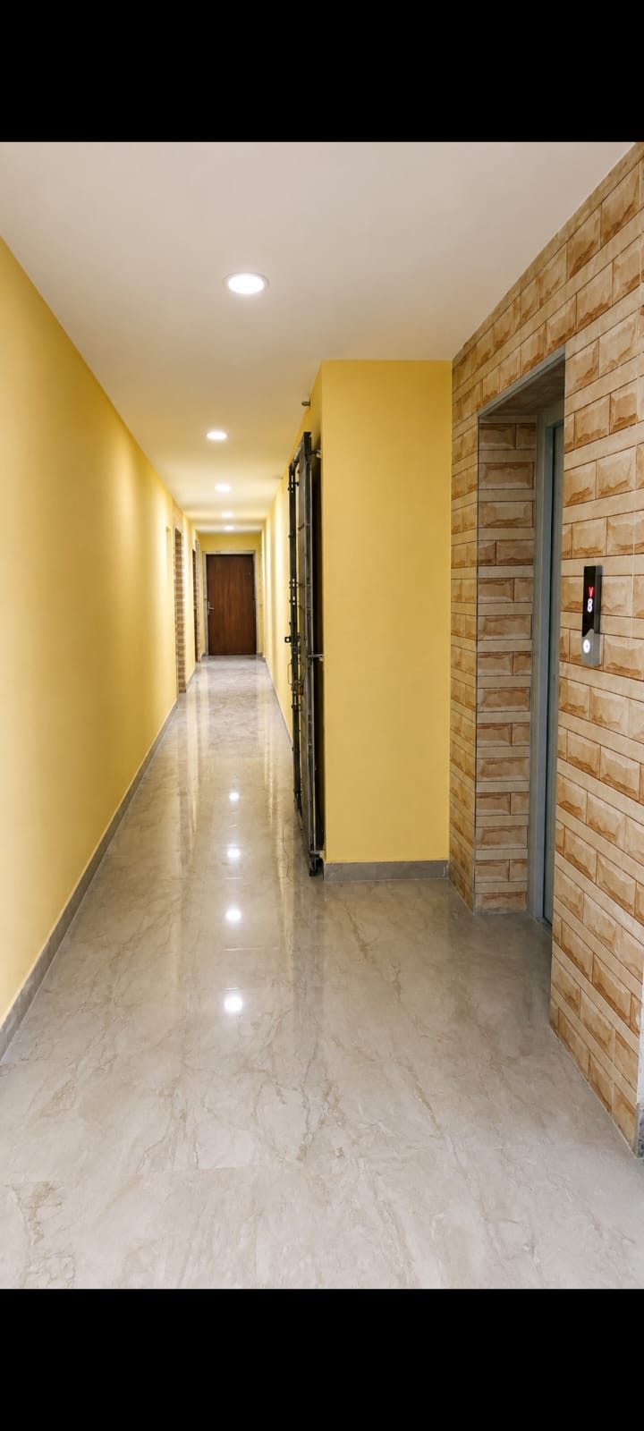 Bright yellow corridor with polished floor and a lift lobby at Krishna Kamdhenu, Kestopur